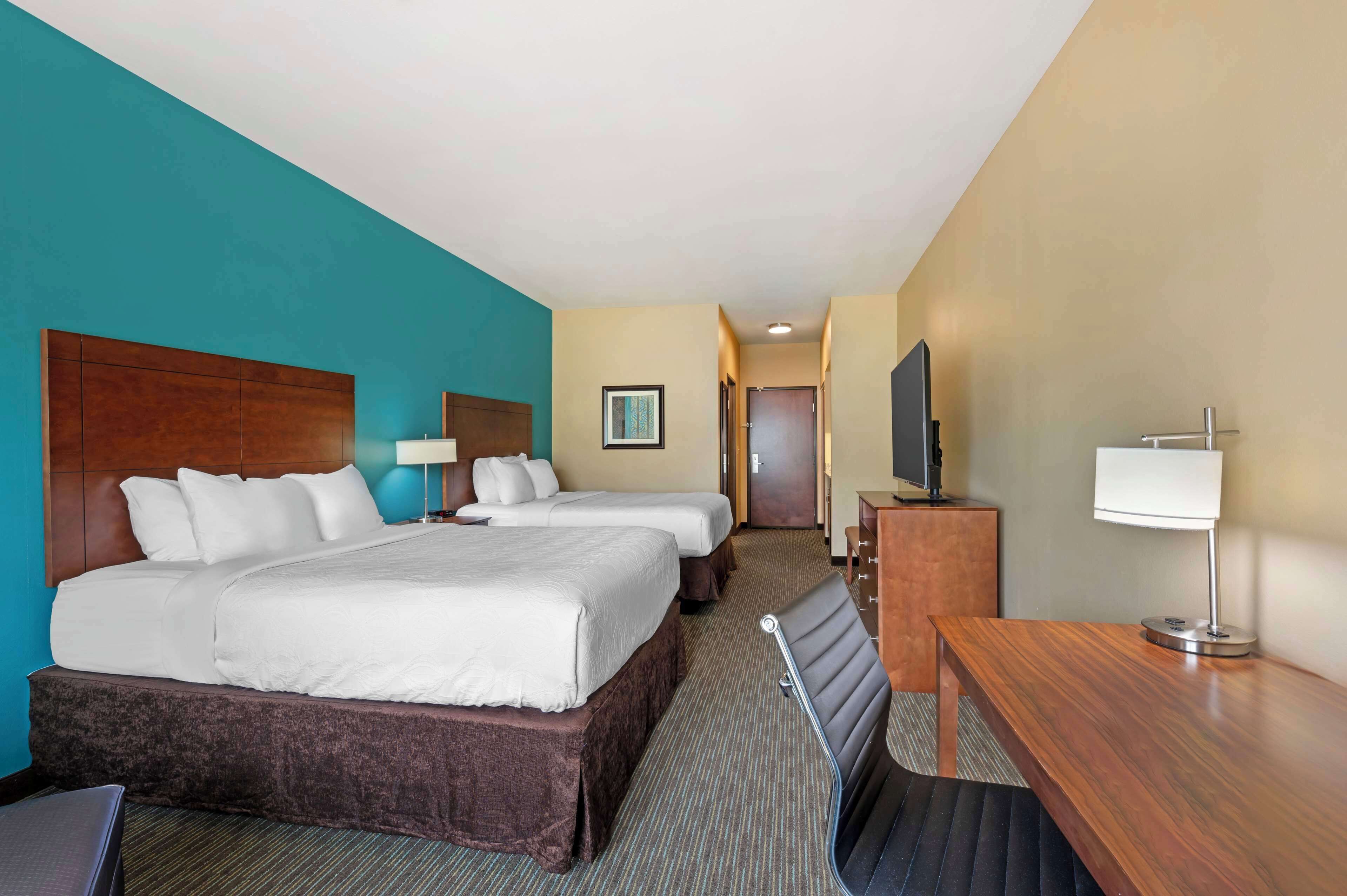 A hotel room with two beds, a desk, a TV, and a bathroom visible in the background.