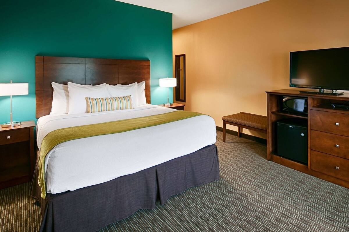 A hotel room with a bed, bedside tables, a TV, a desk, and a chair.