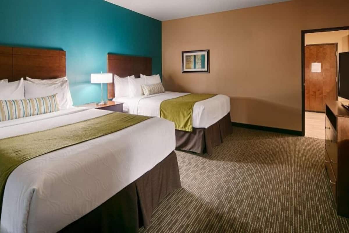 A hotel room with two beds, a television, and a door leading to a hallway.