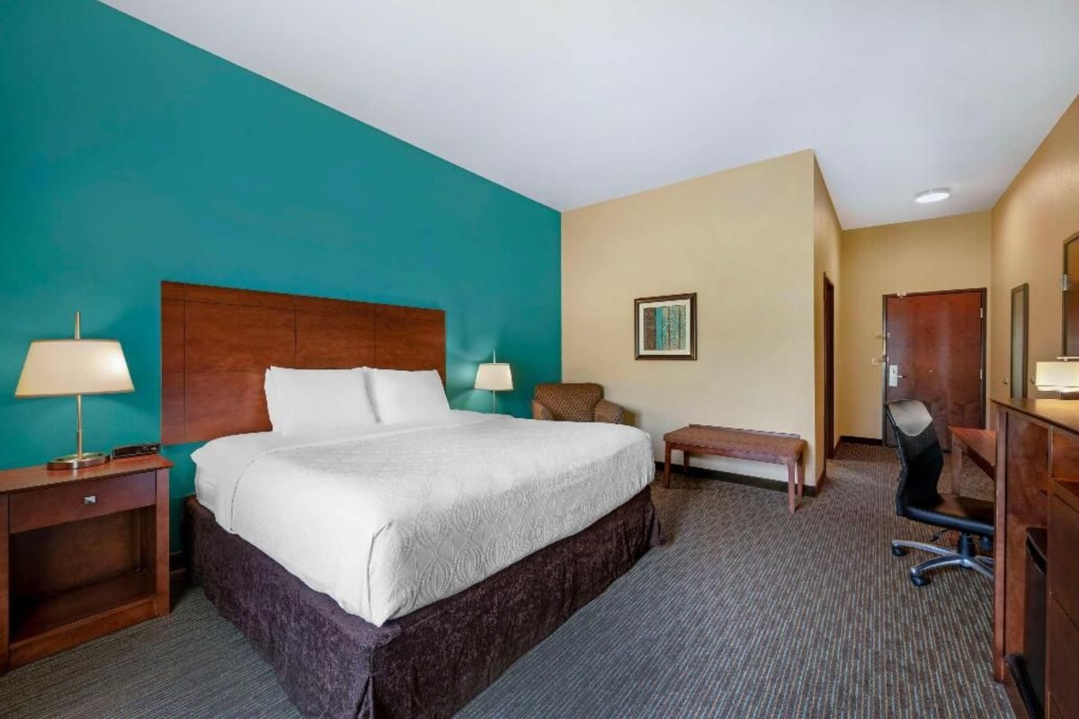 A hotel room with a large bed, a desk, a chair, a bench, and a desk lamp.