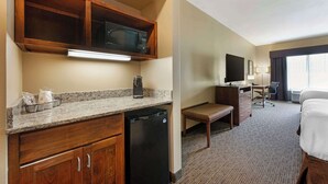 Una habitación de hotel pequeña con kitchenette, cama, escritorio y televisor.