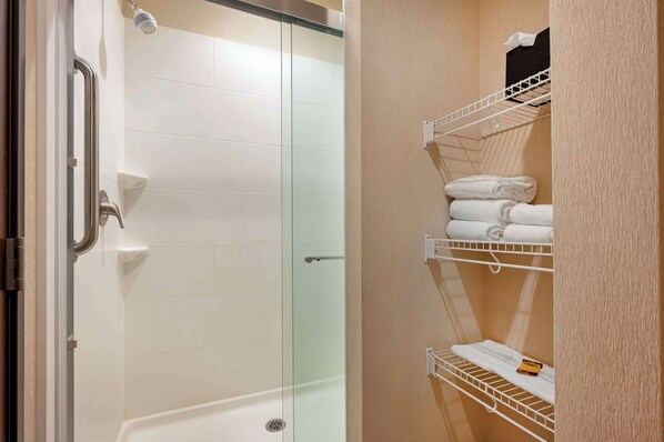 A glass-enclosed shower area with a white tiled wall, a white bathtub, and a towel rack with folded towels.