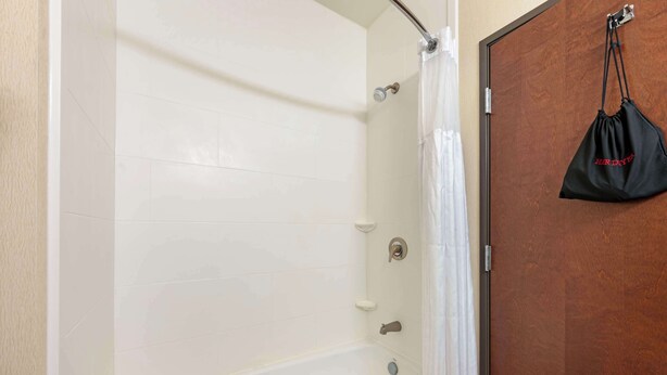 A bathroom with a white bathtub, a wooden door, and a black bag hanging on the door. - Best Western Plus French Lick (French Lick)