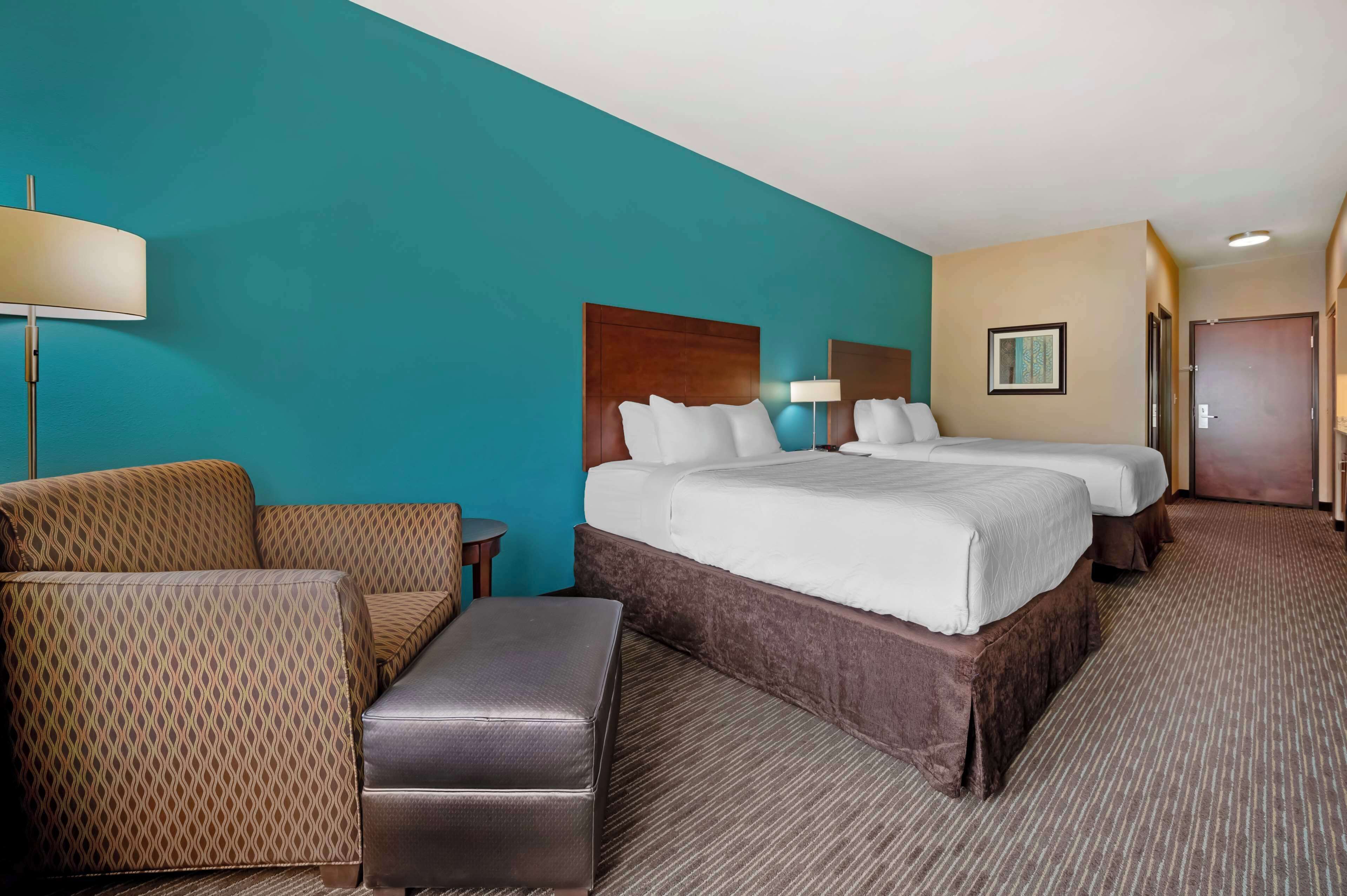 A hotel room with a large bed, two smaller beds, a sofa, a small table, and a bench.