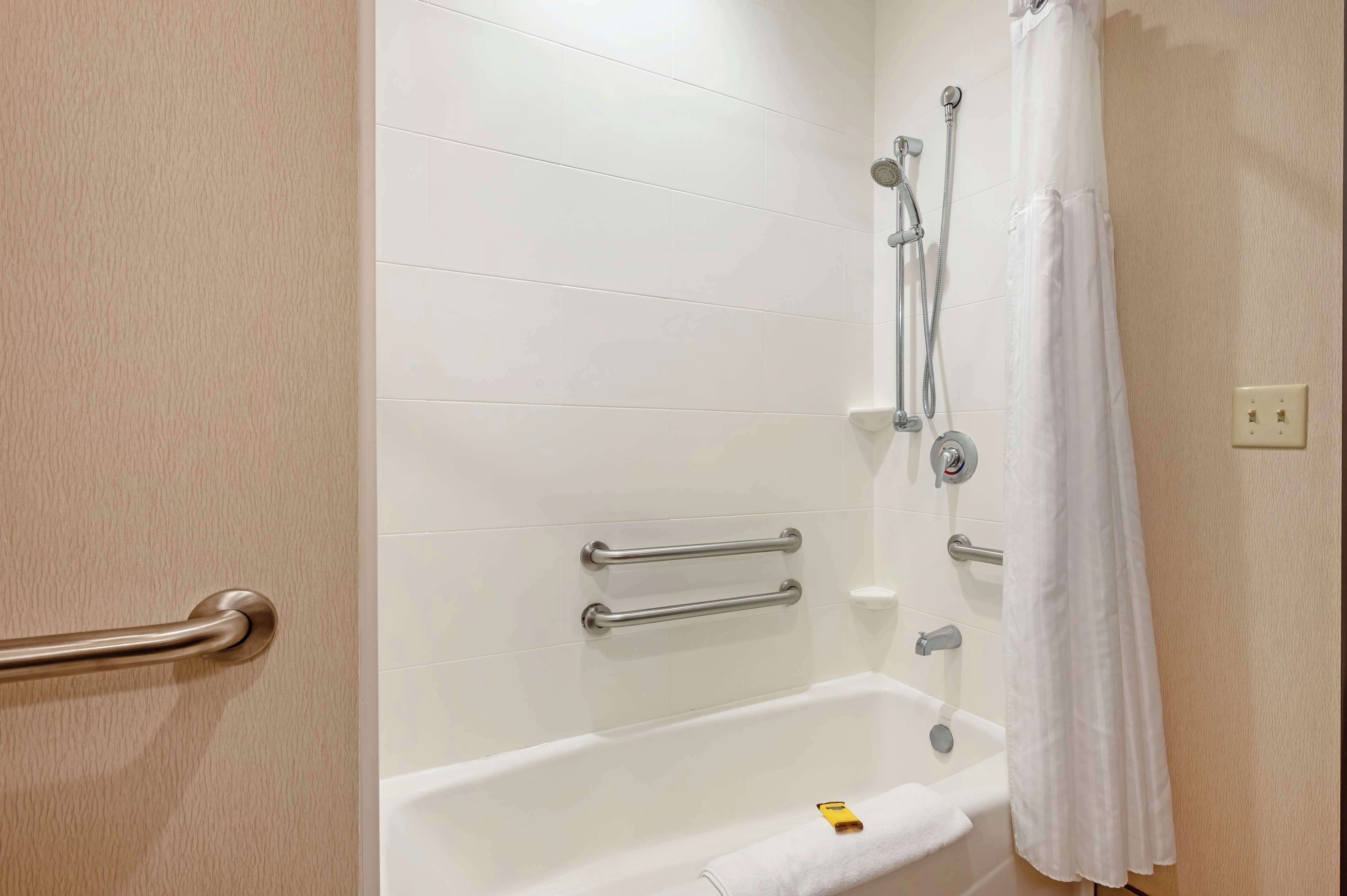 A bathroom with a bathtub, grab bars, a showerhead, and a towel rack.