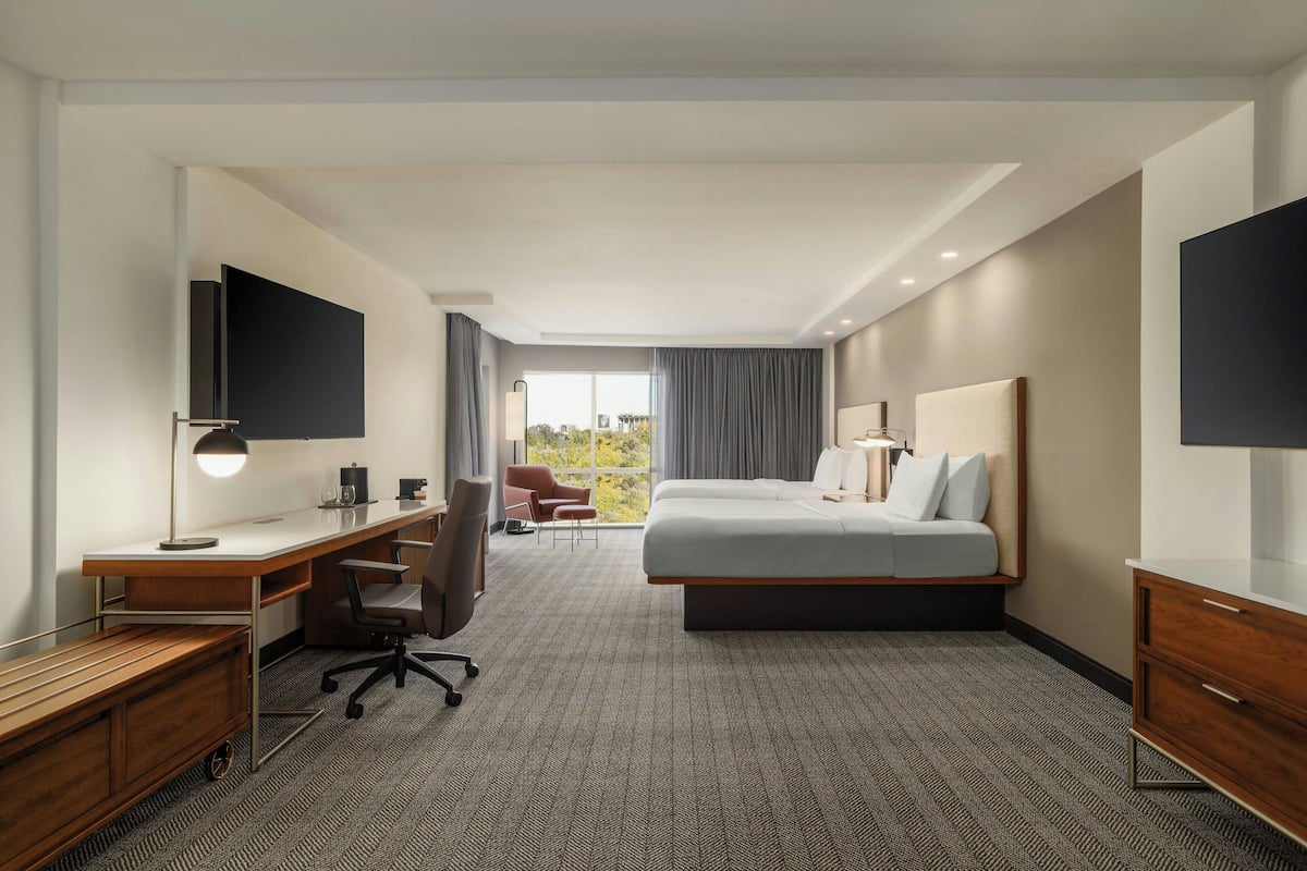 Une chambre d’hôtel avec un lit, un bureau, une chaise et une grande fenêtre.