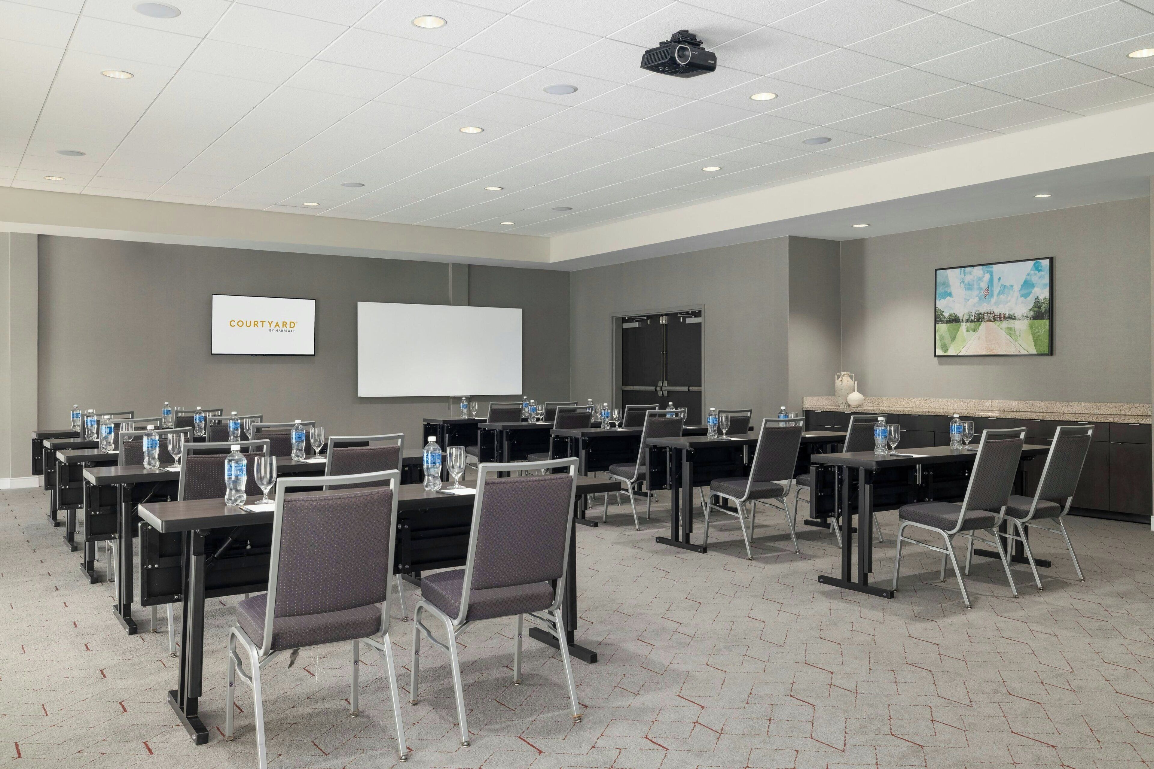 A conference room with multiple tables and chairs, a whiteboard, and a projector on the ceiling.
