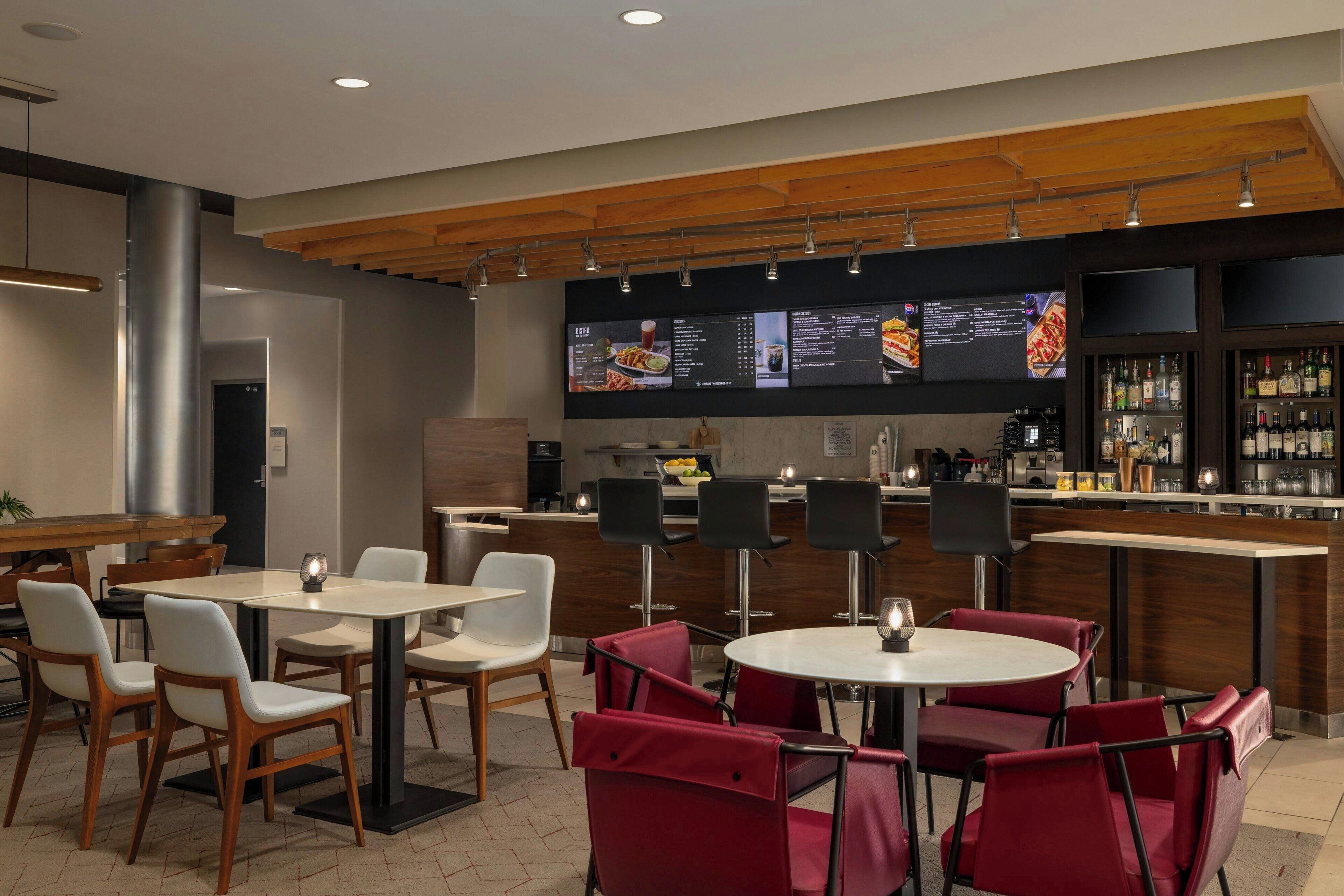 A modern restaurant with a bar area, multiple seating options including round tables and red booths, and a menu display above the counter.