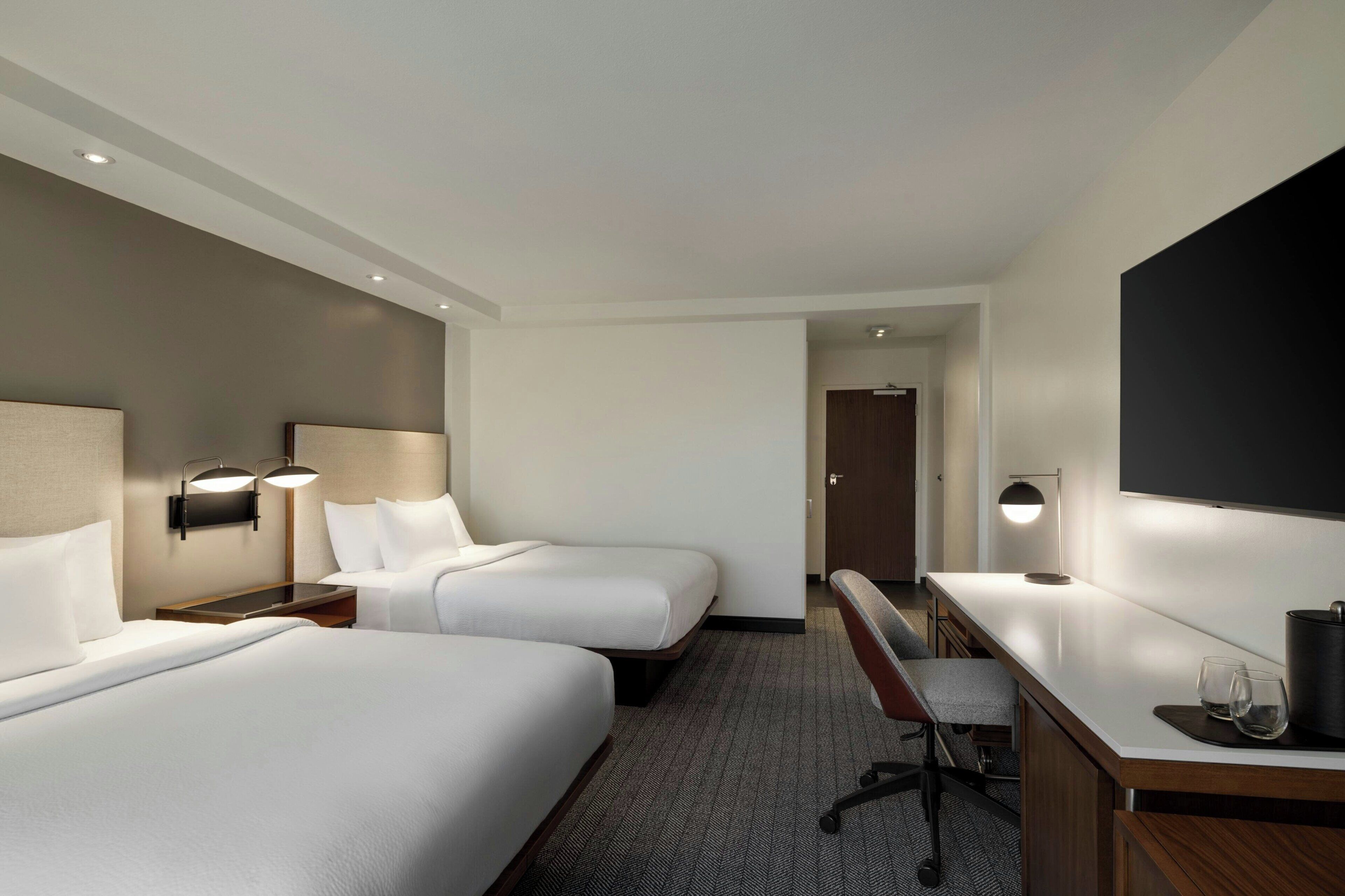 Habitación de hotel con dos camas, un escritorio, una silla y un televisor.