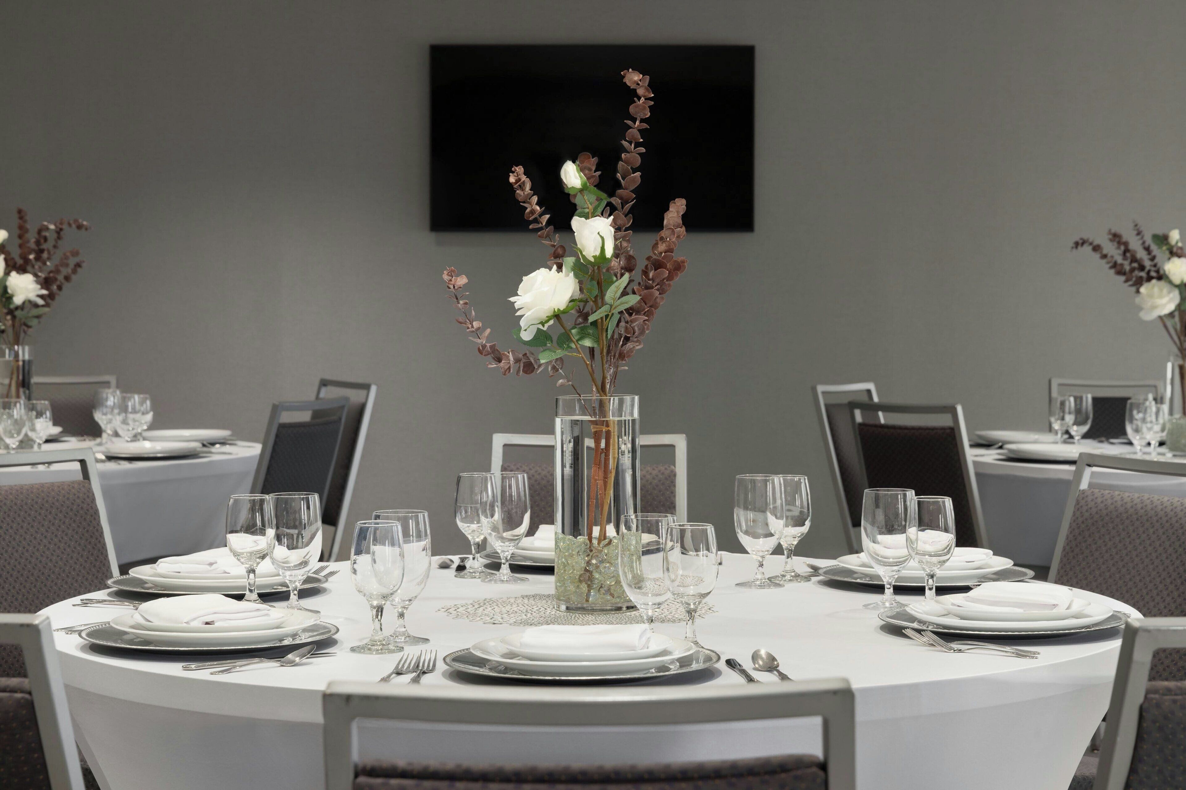 A dining area with round tables set for a meal, each with white tablecloths, plates, cutlery, and glasses.