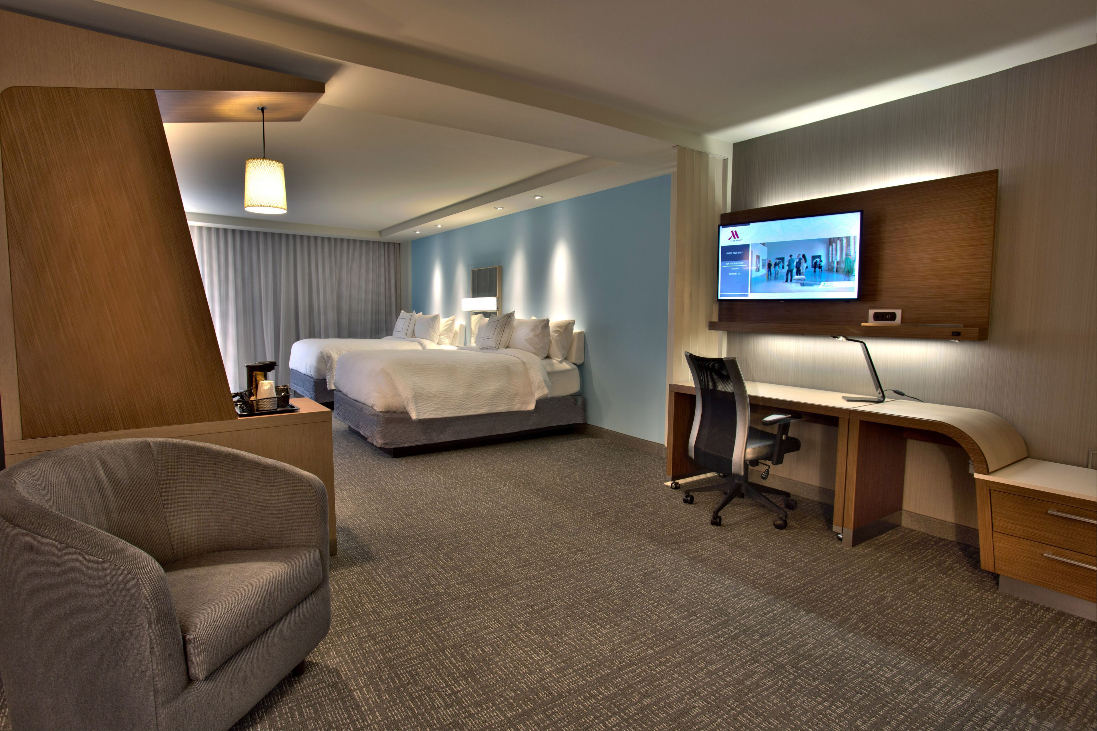 Una habitación de hotel con cama, escritorio, silla y televisor en la pared.
