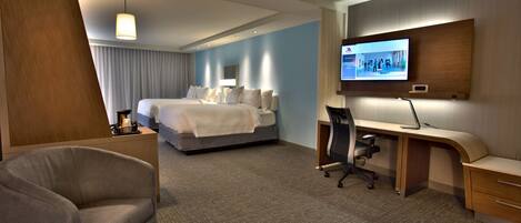 Una habitación de hotel con cama, escritorio, silla y televisor en la pared.