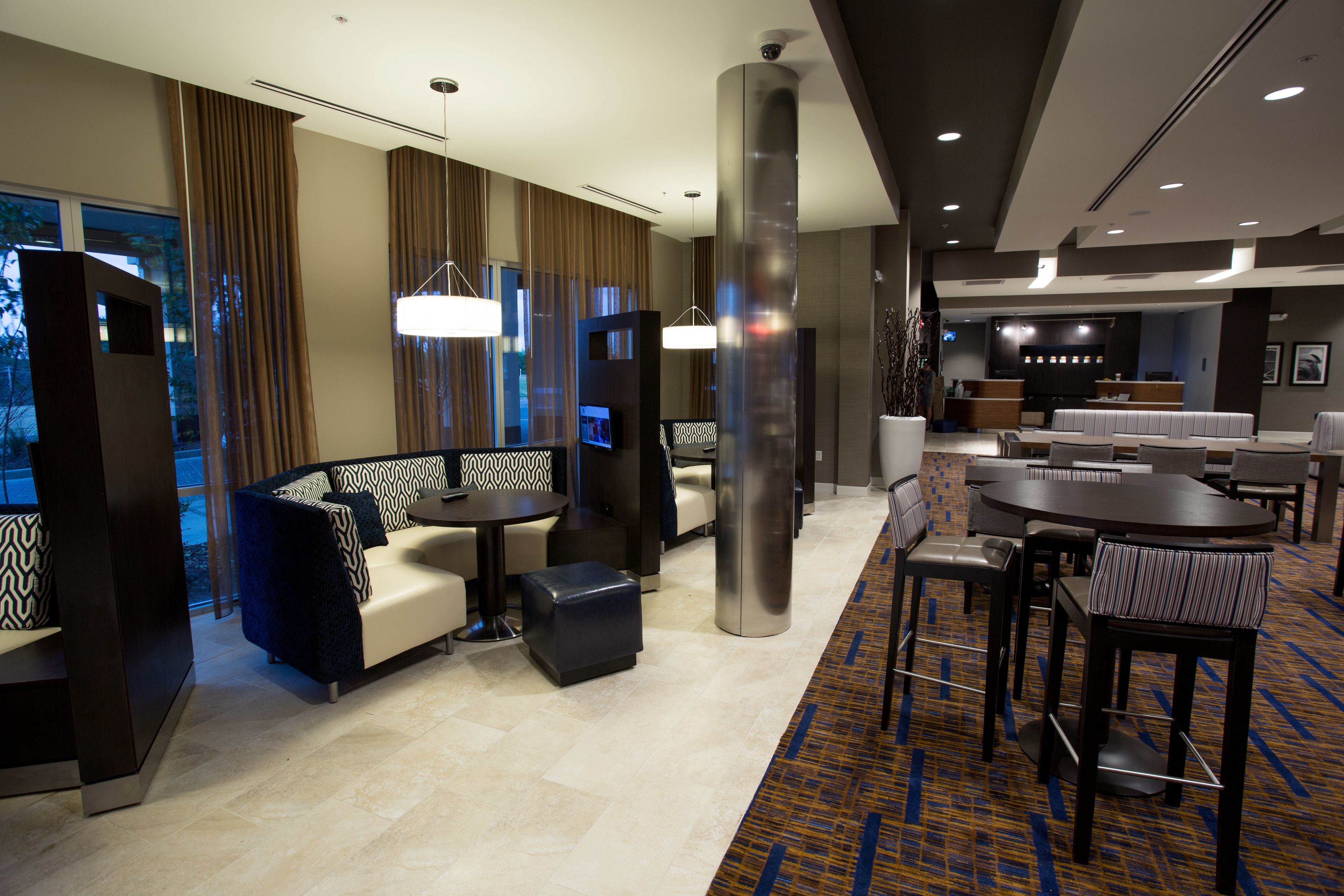 A modern hotel lobby with seating areas, a reception desk, and a large pillar.