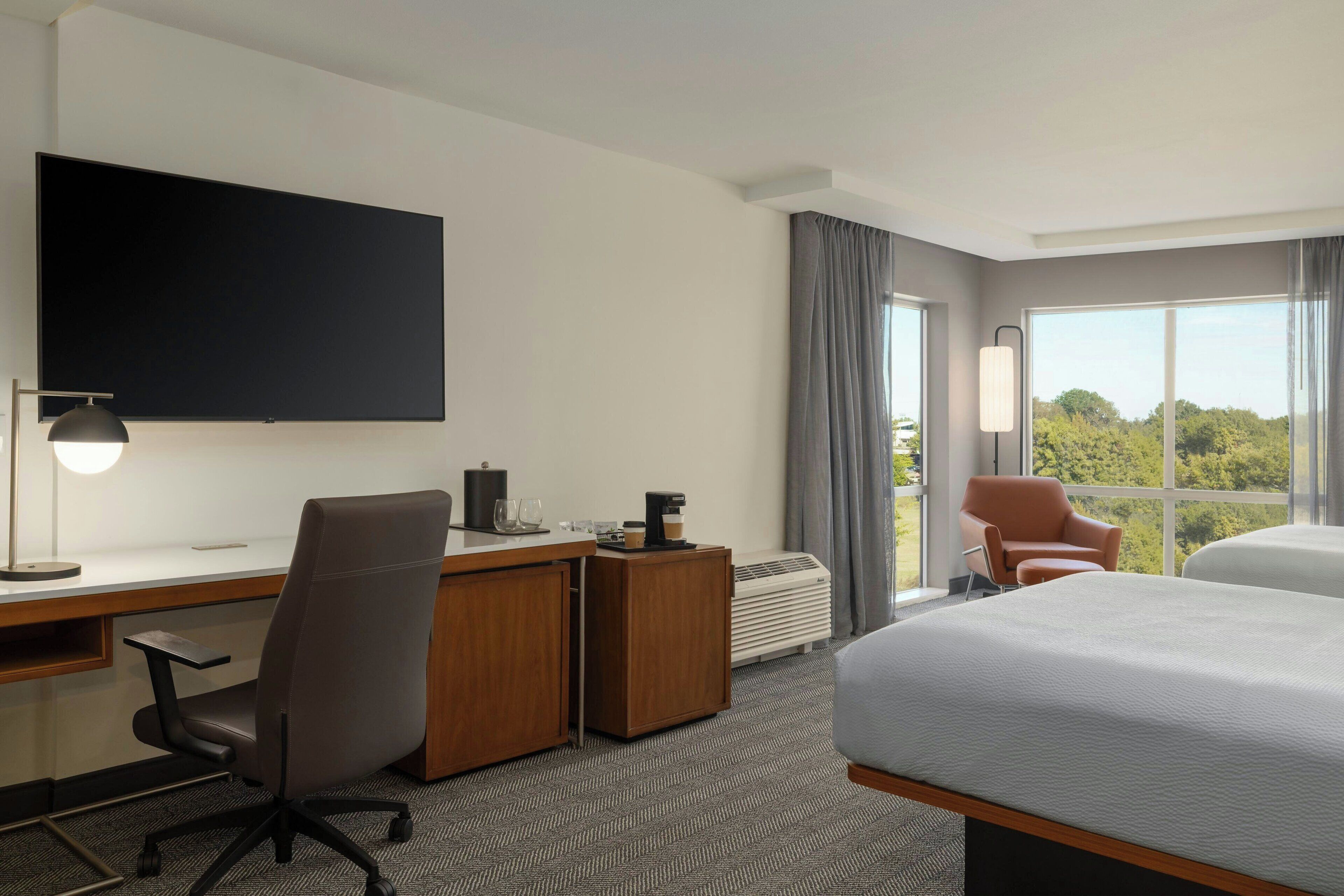 A hotel room with a large bed, a desk with a chair, a flat-screen TV, a coffee maker, and a view of the outdoors.