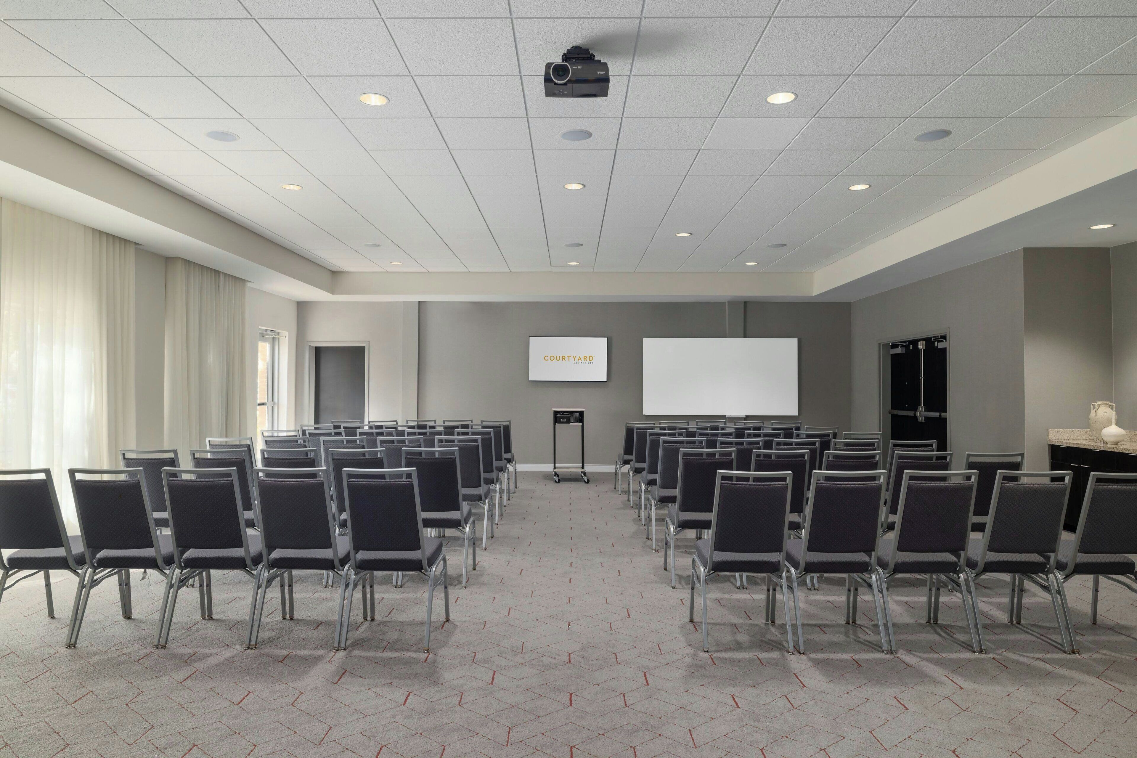 A conference room with rows of chairs, a projector screen, and a whiteboard.