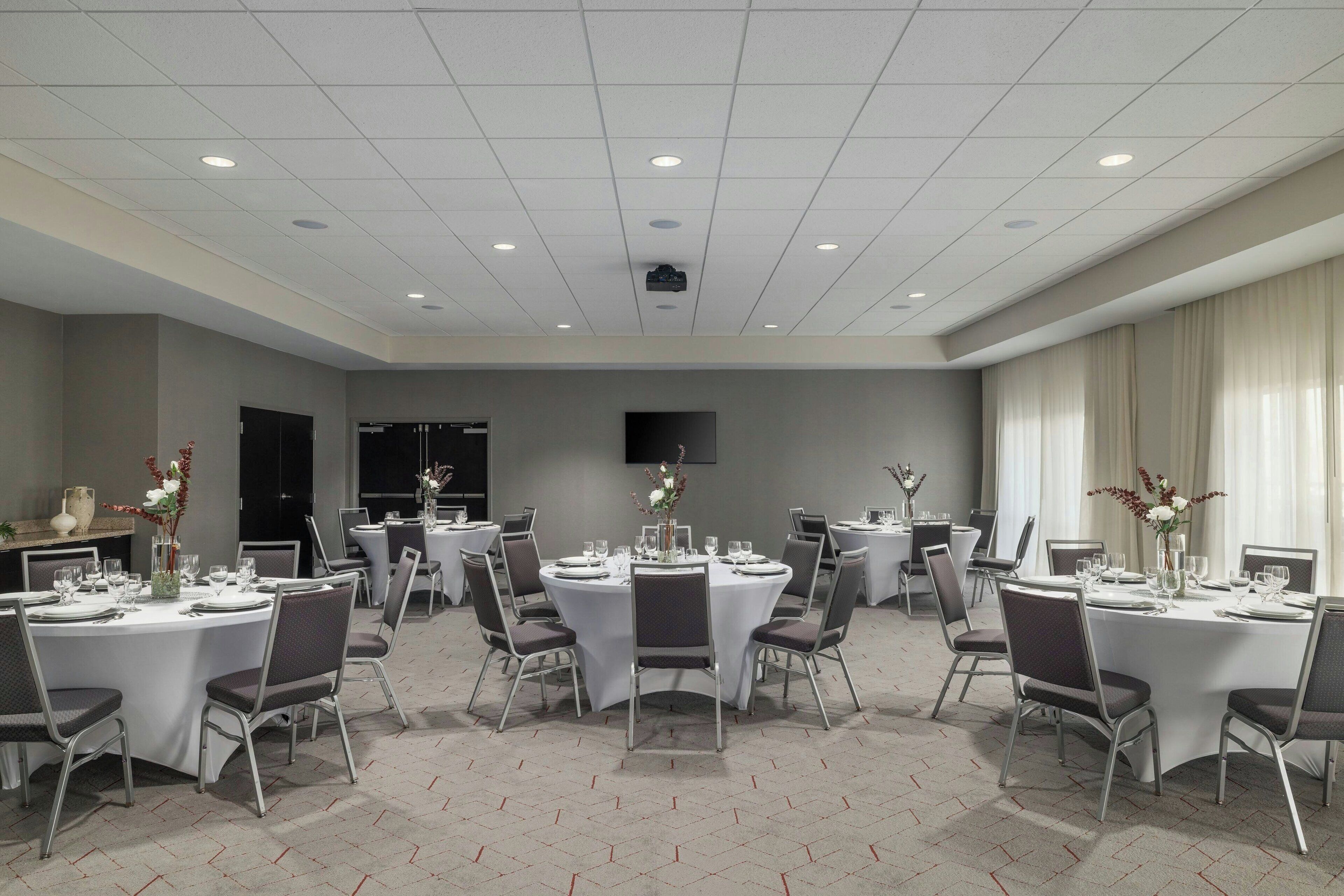 A conference room with round tables, chairs, and a projector screen on the ceiling.