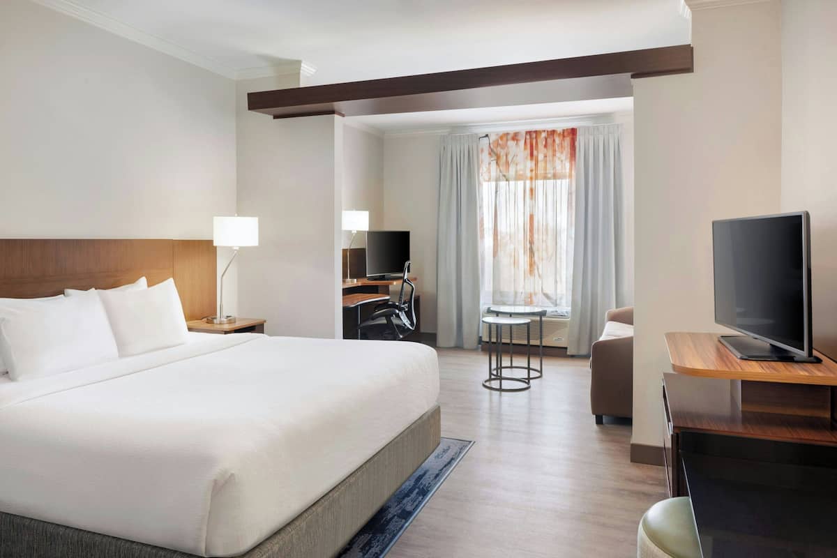 A hotel room with a large bed, a desk with a TV, a chair, and a window with curtains.