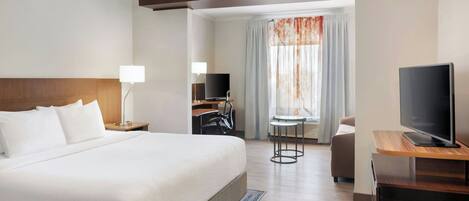 A hotel room with a large bed, a desk with a TV, a chair, and a window with curtains.
