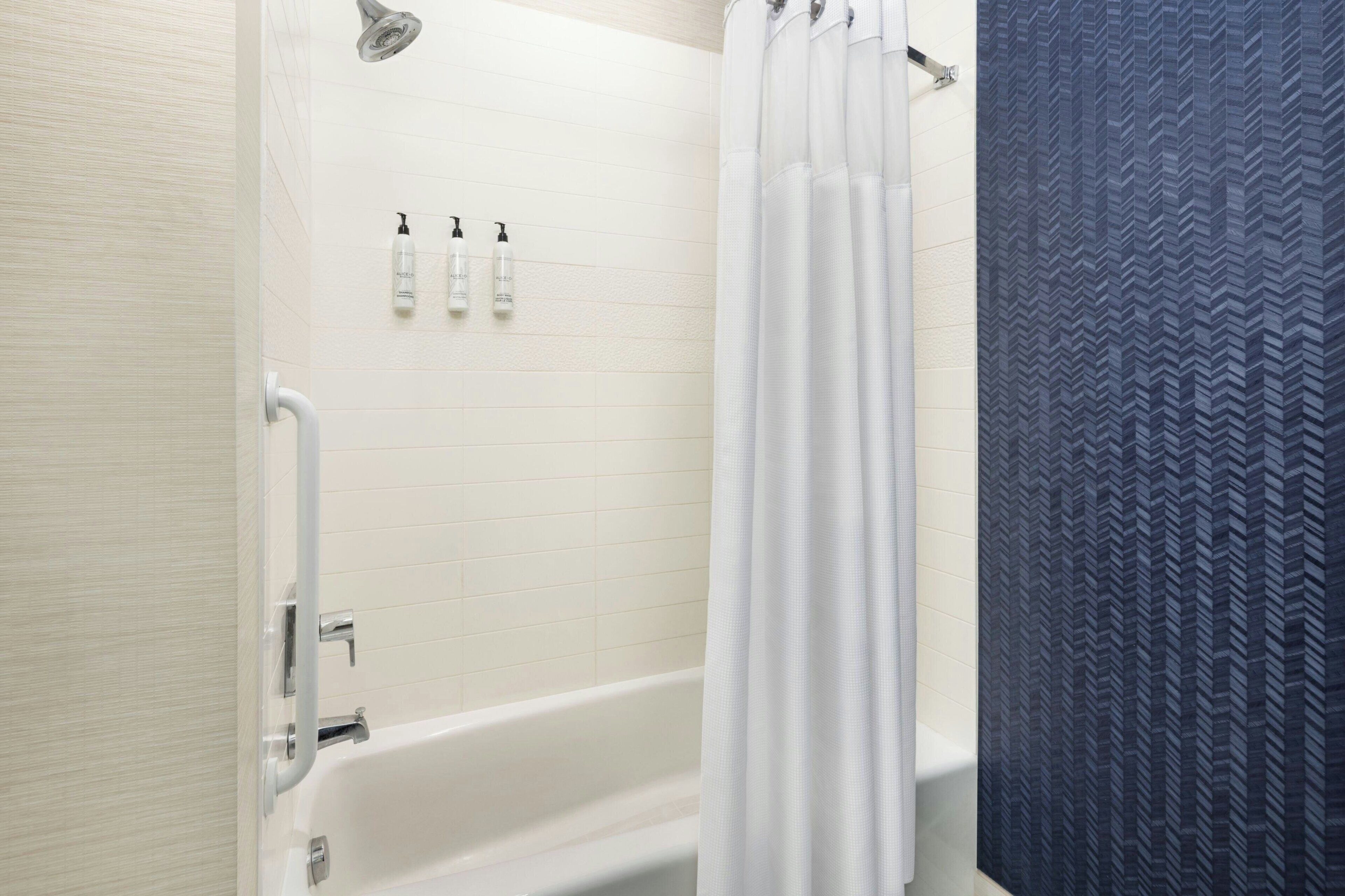 Un baño con bañera, azulejos blancos, un cabezal de ducha y dos botellas de champú en la pared.