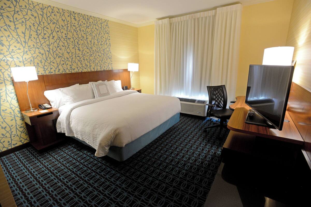 A hotel room with a large bed, two bedside tables with lamps, a television, and a patterned carpet.