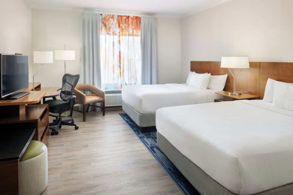 A hotel room with two beds, a desk with a TV, a chair, and a lamp.