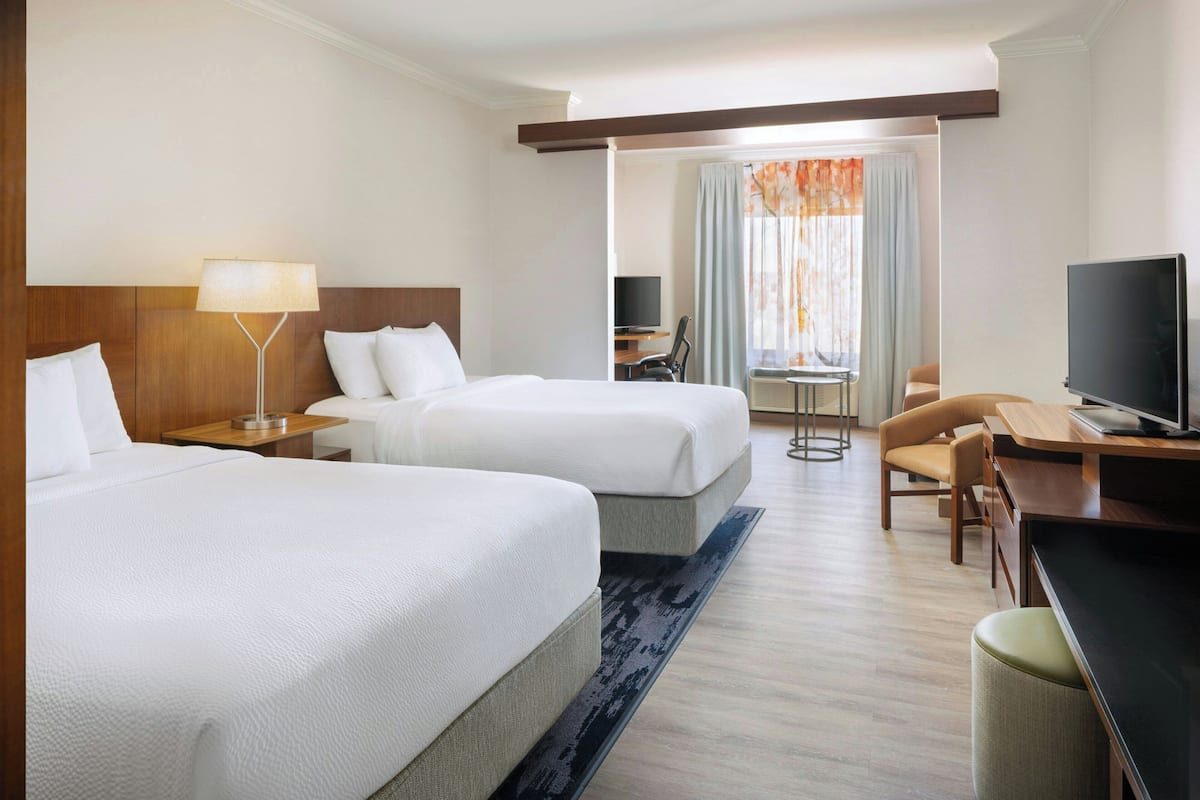 A hotel room with two beds, a desk, a chair, a TV, and a window with curtains.