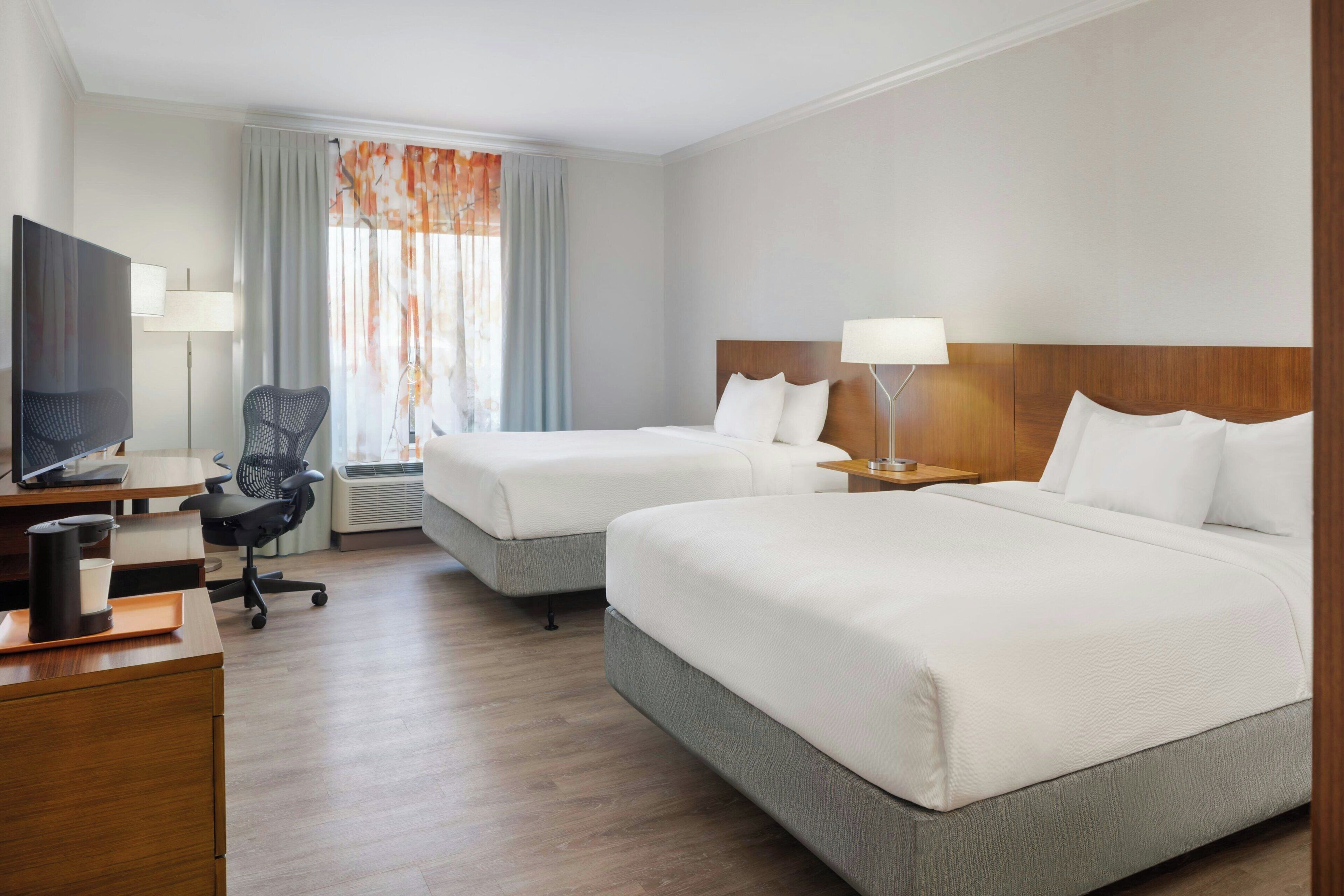 Una habitación de hotel con dos camas, un escritorio con computadora, una silla y un televisor.