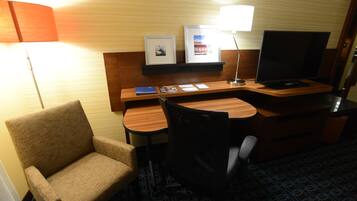 Une chambre d’hôtel avec un bureau en bois, une chaise, un téléviseur, une lampe et des tableaux encadrés accrochés au mur.