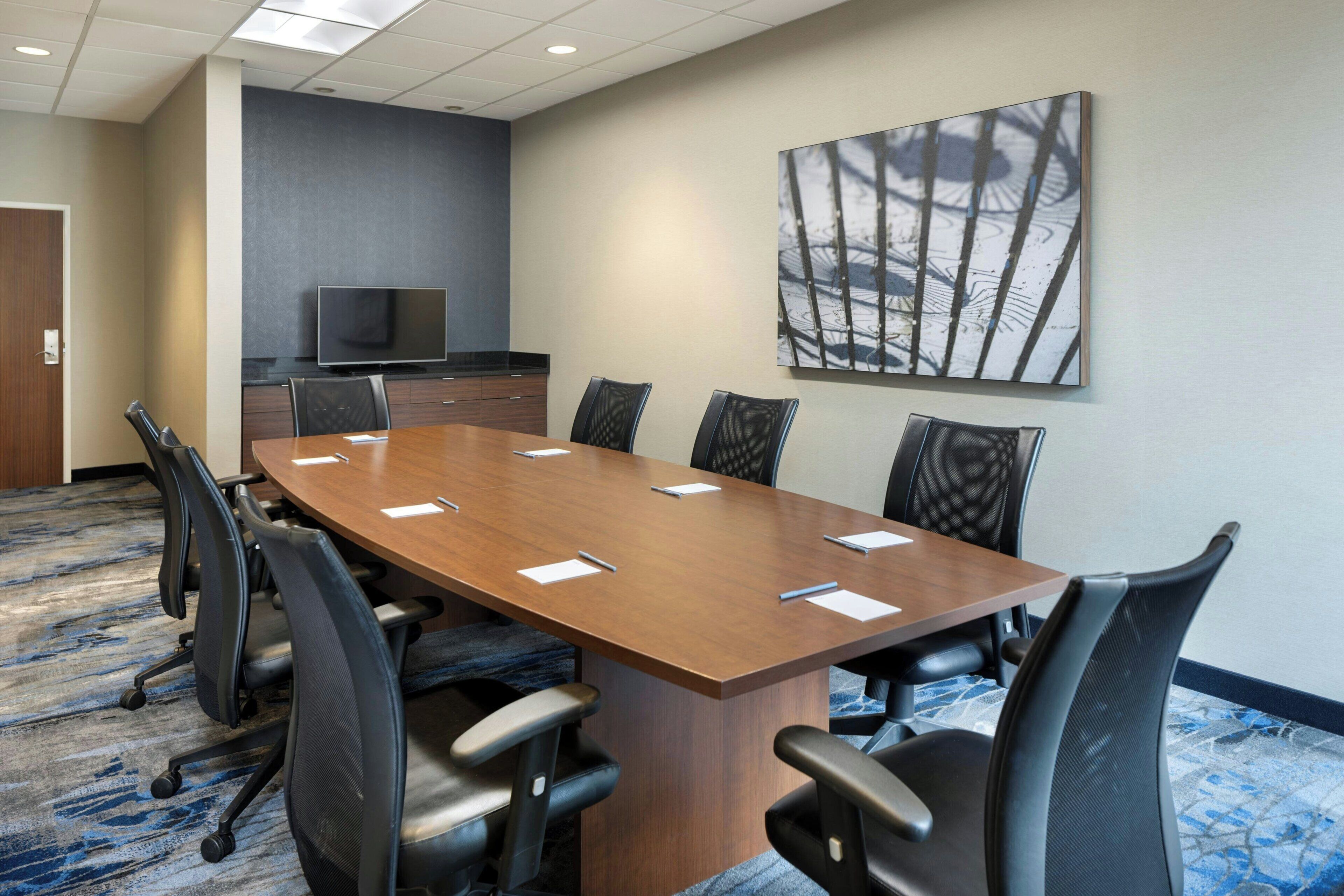 A conference room with a long table, chairs, a flat-screen TV, and a large abstract painting on the wall.