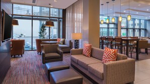 A hotel lobby with a seating area, a dining area, and large windows offering a city view.
