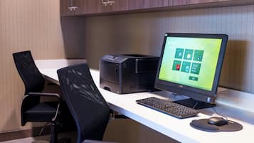 A modern office desk with a desktop computer, a printer, and two office chairs.