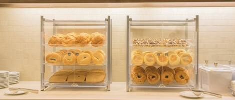 A breakfast buffet with various pastries and bread displayed in clear cases.