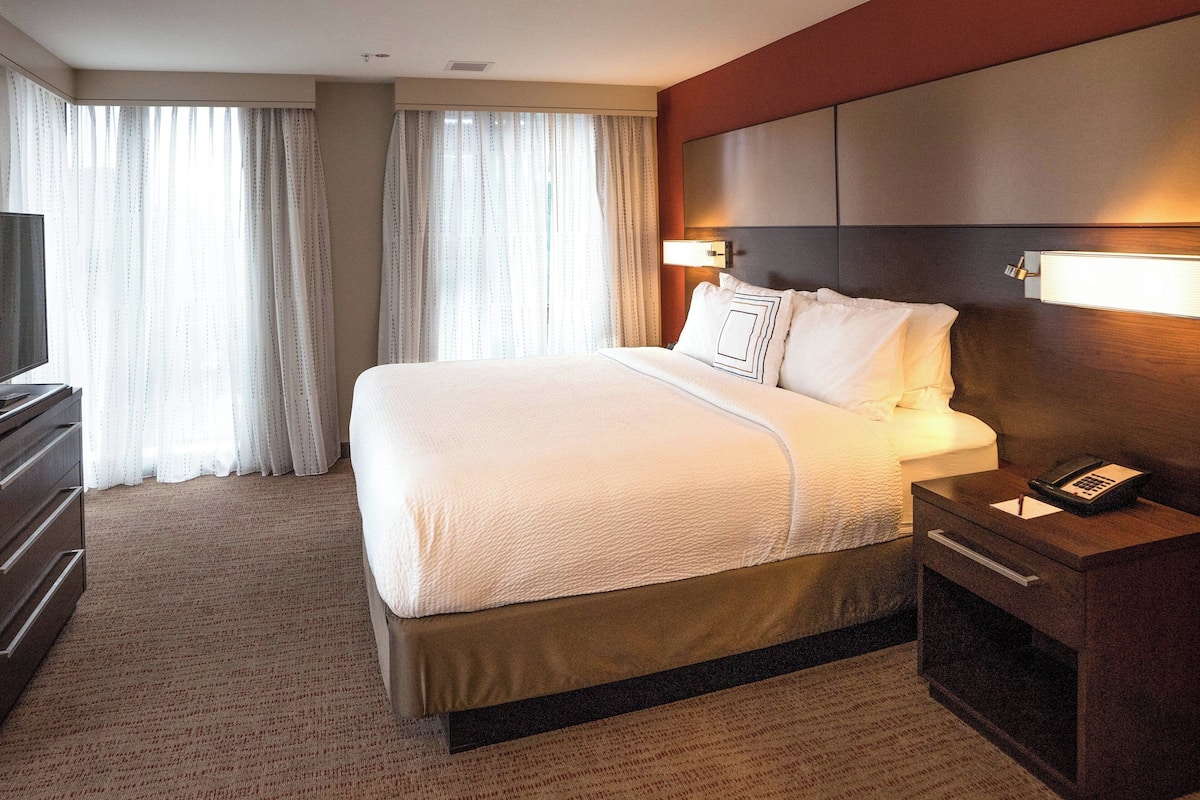 Ein Hotelzimmer mit einem großen Bett, einem Nachttisch mit Telefon, einem Fernseher und einer Kommode.