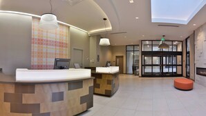 A modern reception area with a curved reception desk, a tiled wall, and a large glass door leading to the lobby.