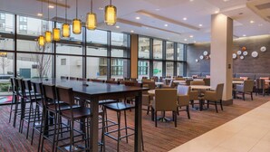 A modern dining area with a large table and chairs, large windows, and a patterned carpet.