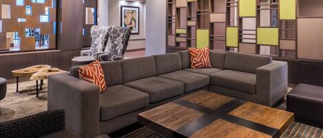 A modern lounge area with a sectional sofa, a wooden coffee table, and a patterned armchair.