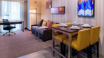 A hotel room with a dining area, a sofa, a desk, and a chair.