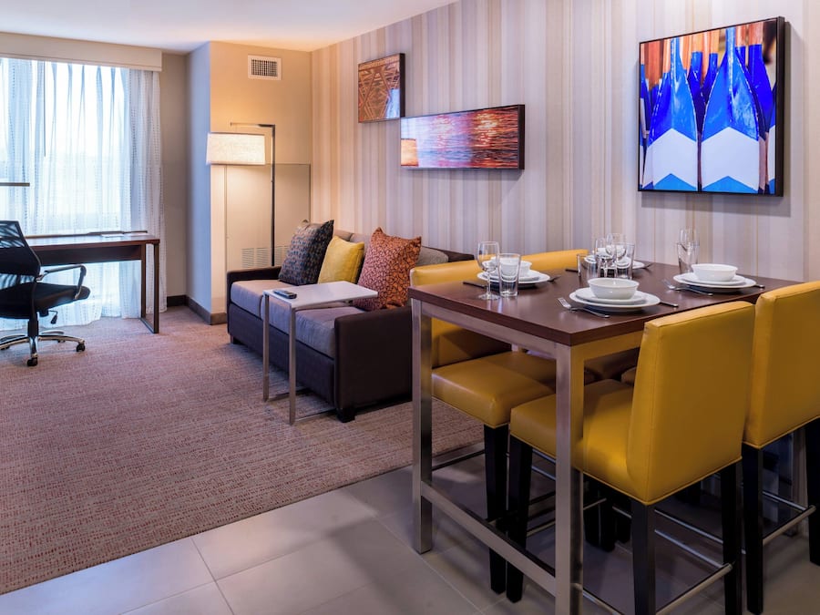 A hotel room with a dining area, a sofa, a desk, and a chair.
