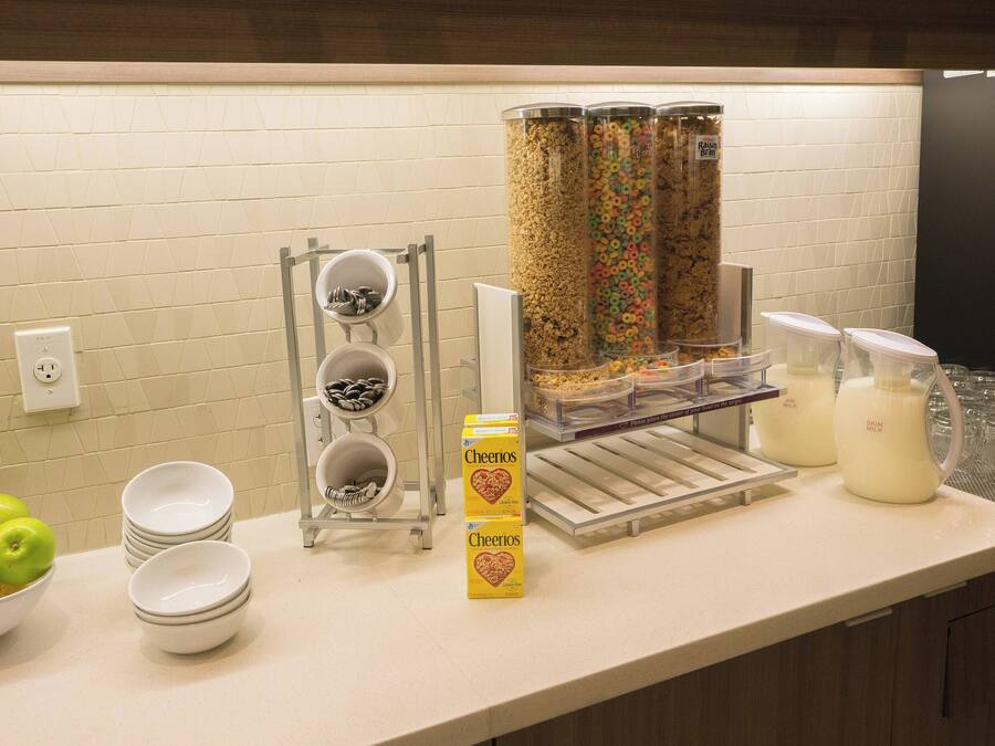 A breakfast bar with Cheerios cereal, milk, and a bowl of fruit.