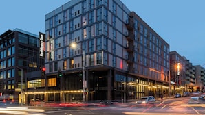 A modern hotel with a glass facade, multiple floors, and a prominent entrance.