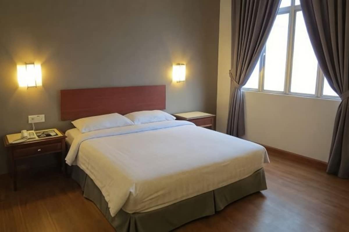 Una habitación de hotel con cama, mesitas de noche, lámparas y un ventanal con cortinas.