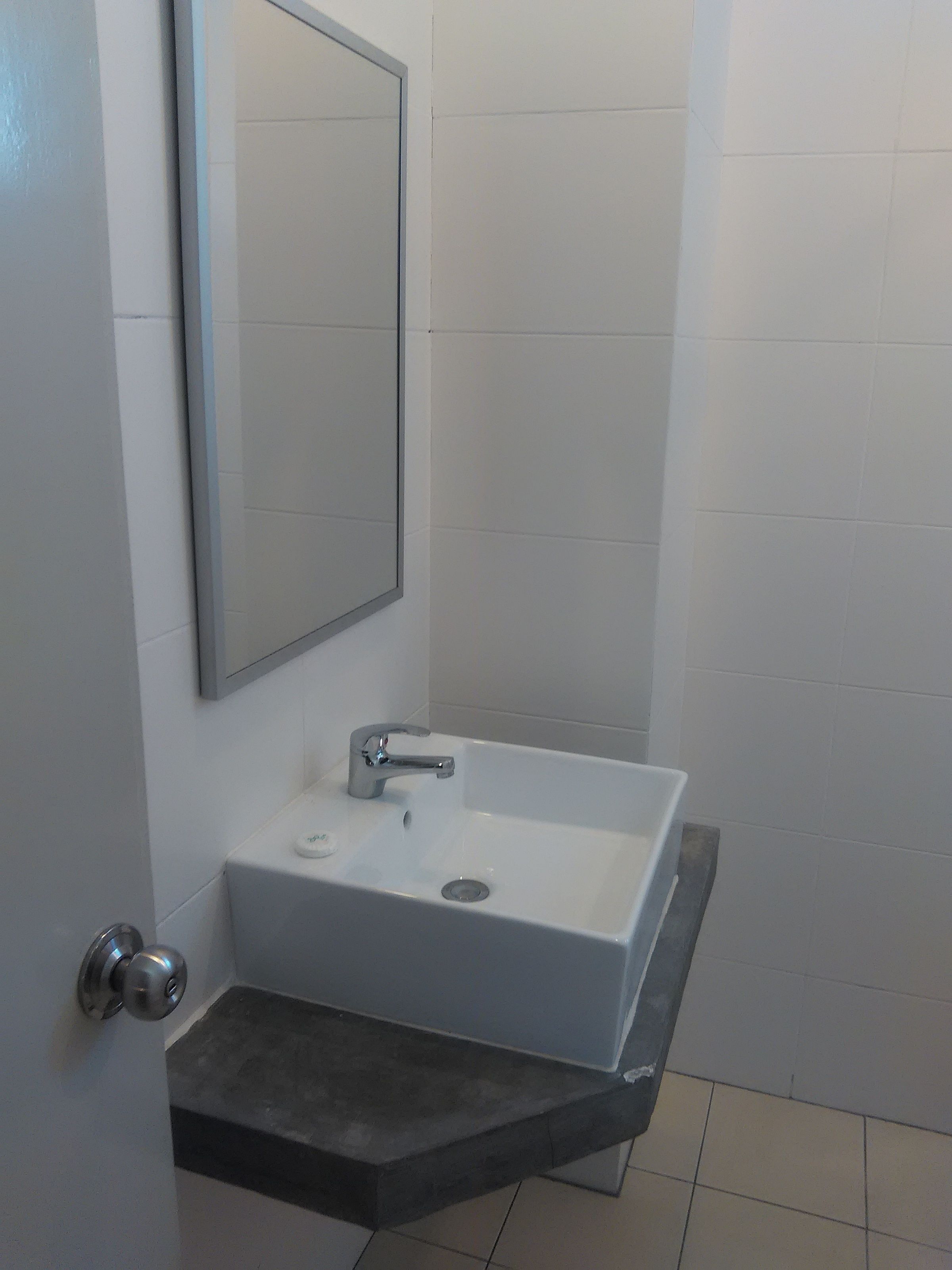 Un baño con un lavamanos blanco, un espejo y una puerta con pomo plateado.