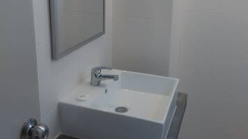 Un baño con un lavamanos blanco, un espejo y una puerta con pomo plateado.