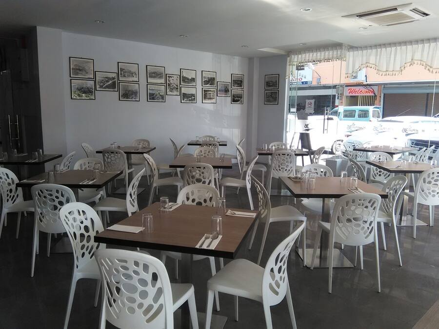 Un restaurante con sillas y mesas blancas, cuadros en la pared y vistas a vehículos estacionados afuera.