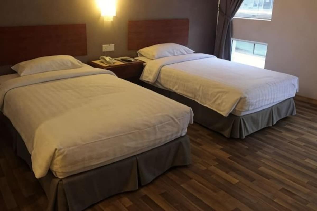 Habitación de hotel con dos camas, piso de madera, una mesita de noche con teléfono y una ventana con cortinas.