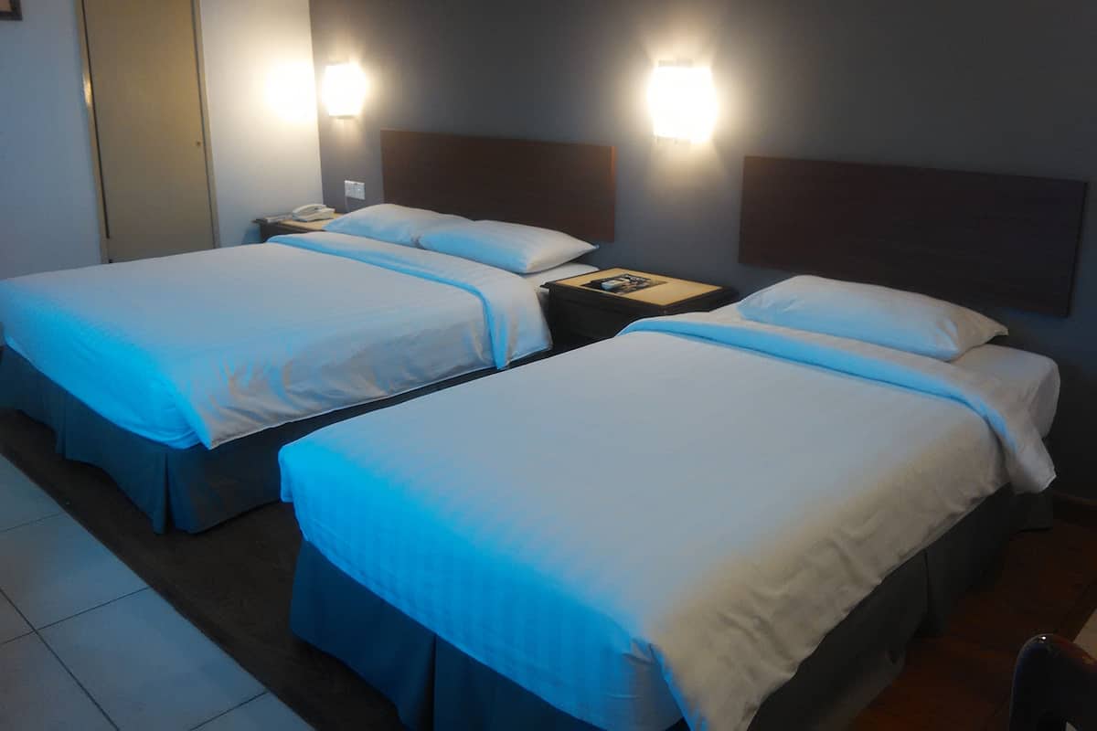 A hotel room with two single beds, each with a headboard, a bedside table with a lamp, and a wall-mounted light fixture.