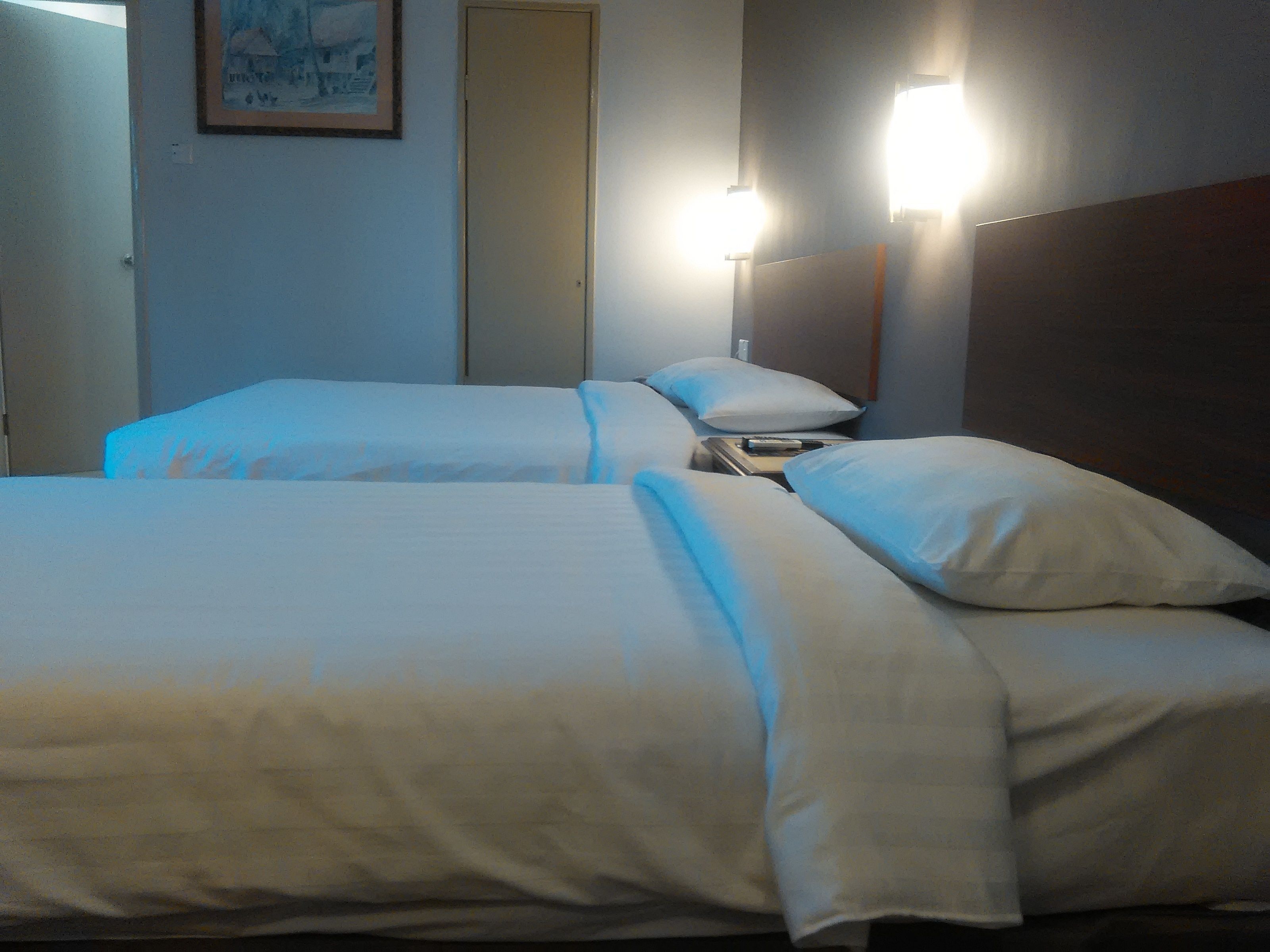 A hotel room with two beds, a nightstand, and a wall-mounted lamp.