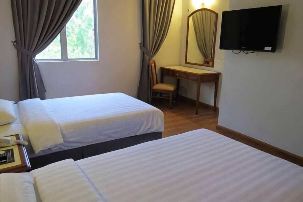 A hotel room with two beds, a desk, a chair, a television, and a window with curtains.