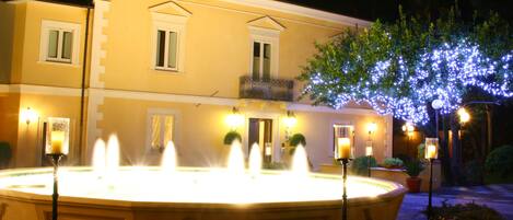 A fountain with multiple water jets in front of a building with balconies and windows.