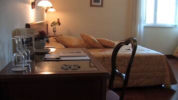 A hotel room with a bed, a desk with a laptop, a vase with flowers, and a lamp.